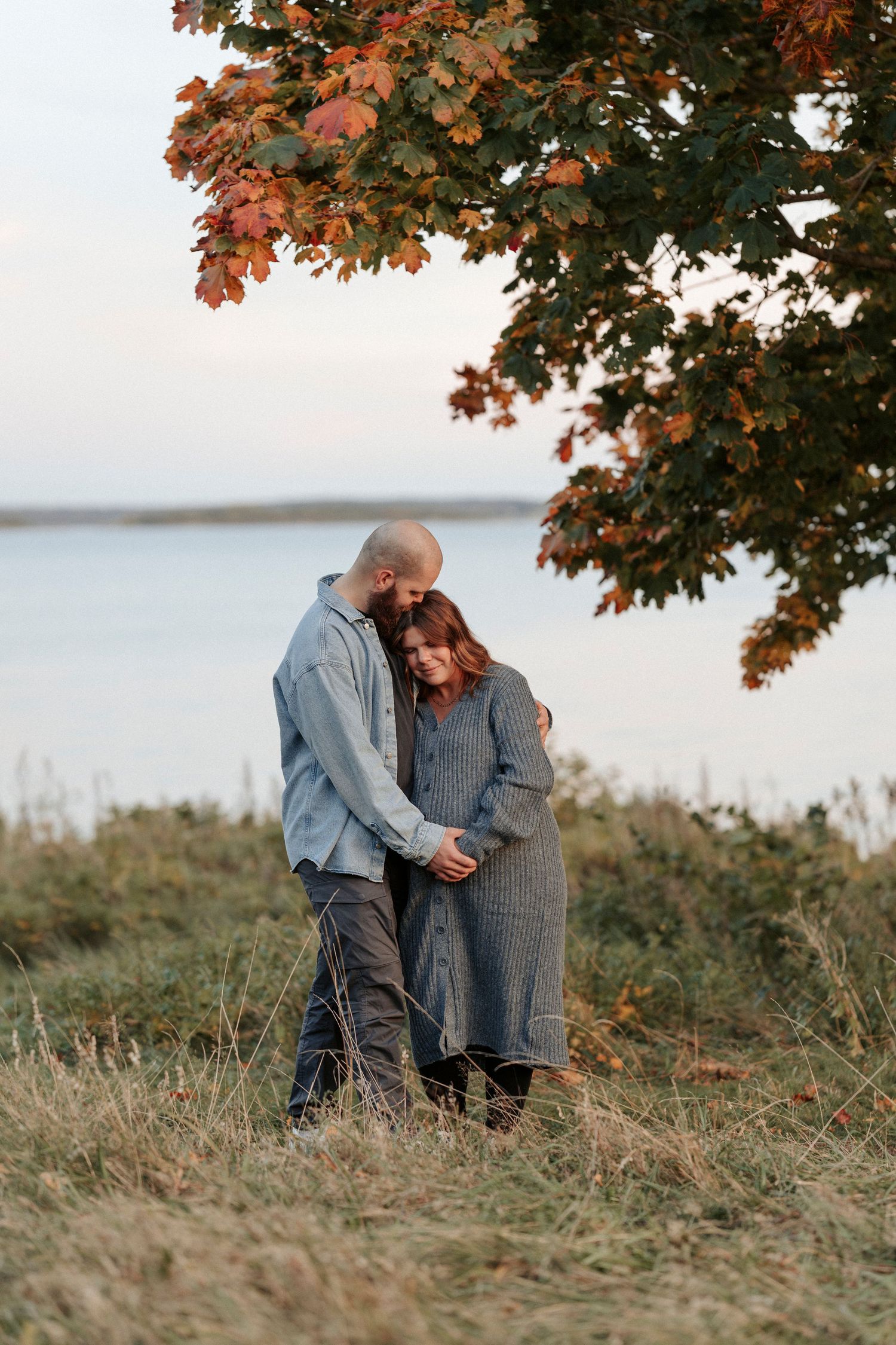 Ett par som väntar barn som står och håller om varandra vid havet. De håller varandras hand på kvinnans mage.