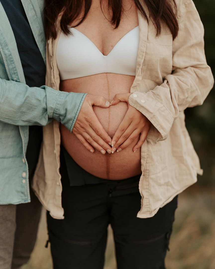 detaljbild på en gravid kvinna och hennes mage, kvinnan och mannen håller sina händer på magen och skapar tillsammans ett hjärta