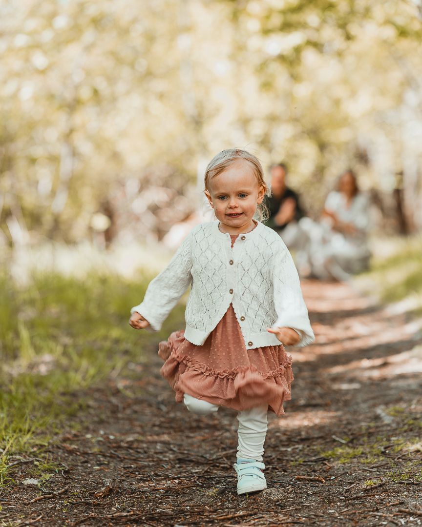 En liten flicka springer på en stig i Särö, hon springer mot kameran och man kan se hennes föräldrar som sitter på huk i bakgrunden