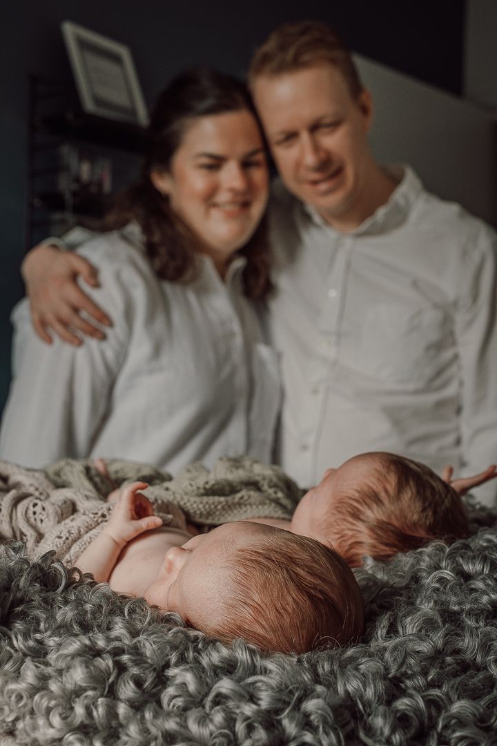 En mamma och en pappa som står och håller om varandra, de står och kollar på sina två barn som ligger och sover på en fäll framför dom