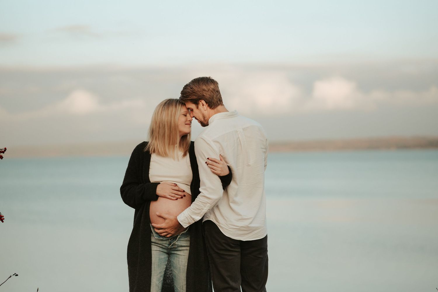 Par som väntar barn som står vid havet. Mannen står med ryggen mot kameran och kvinnan mot kameran, de håller om varandra