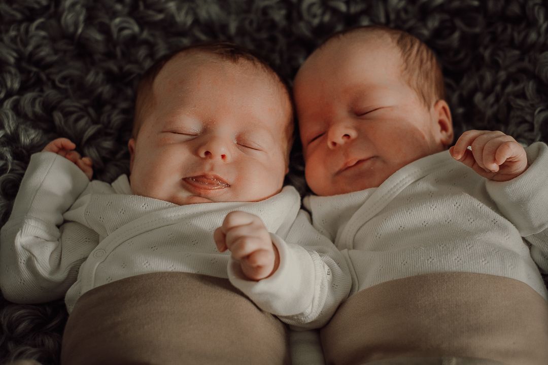 Tvillingbebisar som ligger bredvid varandra, huvud mot huvud och sover. De har likadana kläder på sig.
