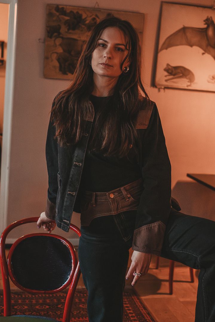 Kvinna som har på sig svarta jeanskläder står lutad mot en stol.