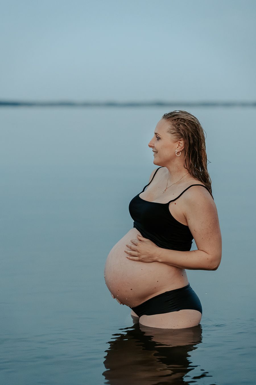 Gravid kvinna står i vattnet i Kungsbacka. Magen är bar och hon håller ena handen på magen och blickar ut över havet