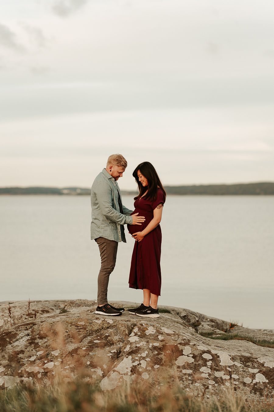 Ett par som väntar barn som står på en klippa vid havet i Kungsbacka. De står mot varandra och håller om magen