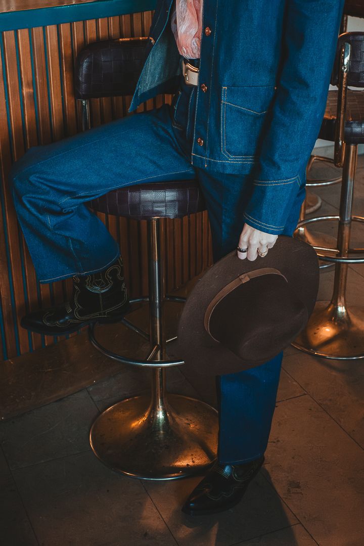 En detaljbild på ett par cowboy boots och en cowboy hat. En kvinna håller hatten i handen och håller den längst med sidan av sin kropp.