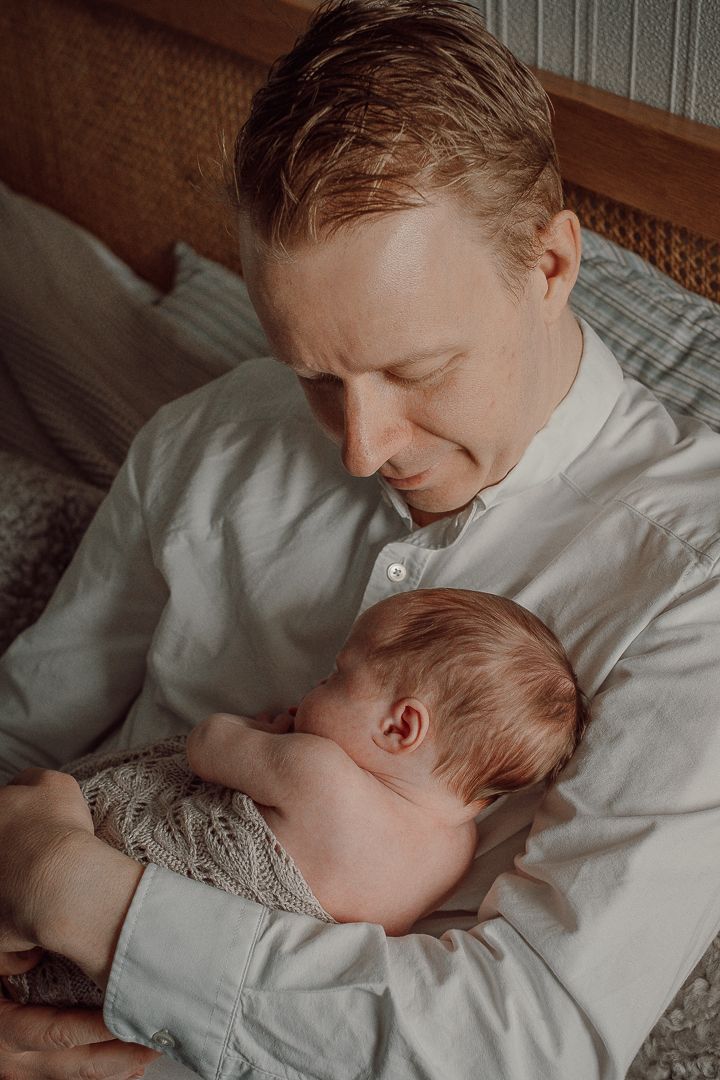 En pappa som har sitt barn i famnen, han tittar ner på sitt barn. Man ser bakhuvudet och örat på spädbarnet.
