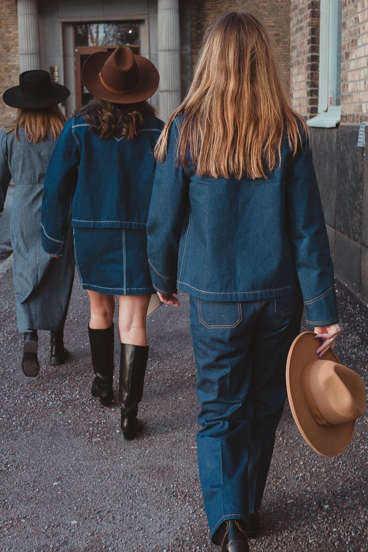 Tre kvinnor som går på rad med ryggarna mot kameran. Den sista kvinnan håller i en cowboy hat.