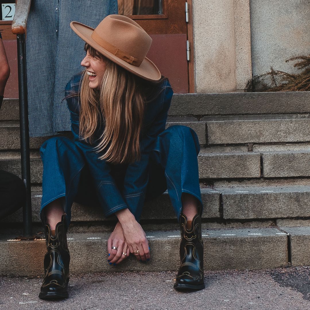 Kvinna som sitter på en trappa, hon har på sig cowboy hatt och boots och jeanskläder