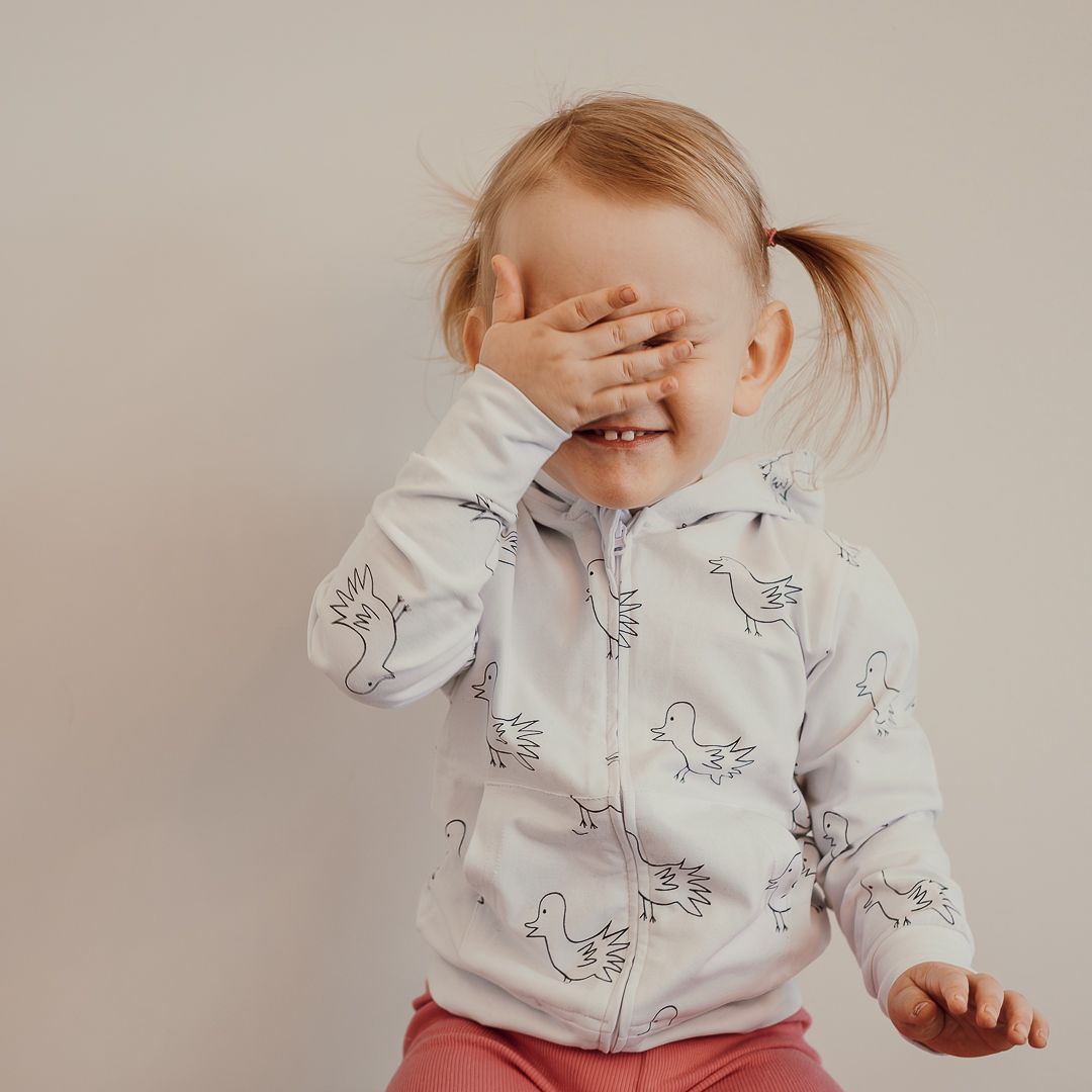 Liten flicka som sitter ner, hon har på sig en vit tröja och håller händerna för ögonen