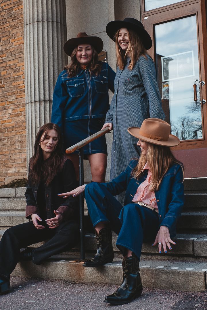 En gruppbild på fyra kvinnor som har på sig cowboy hattar och cowboy inspirerade kläder. De spelar luftgitarr och dansar. två sitter ner