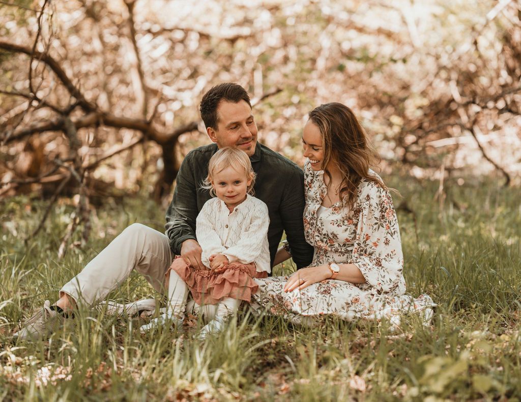 Familj sitter i gräset i Särö. Pappan har sin dotter i knät och mamman sitter bredvid. Mamman kollar på barnet och pappan kollar på mannan.