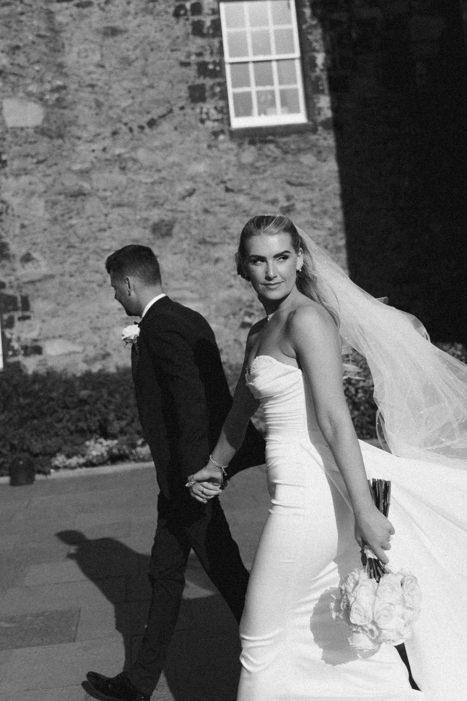 Black and white wedding photo sequence showing playful interaction between bride and groom outdoors by stone wall.