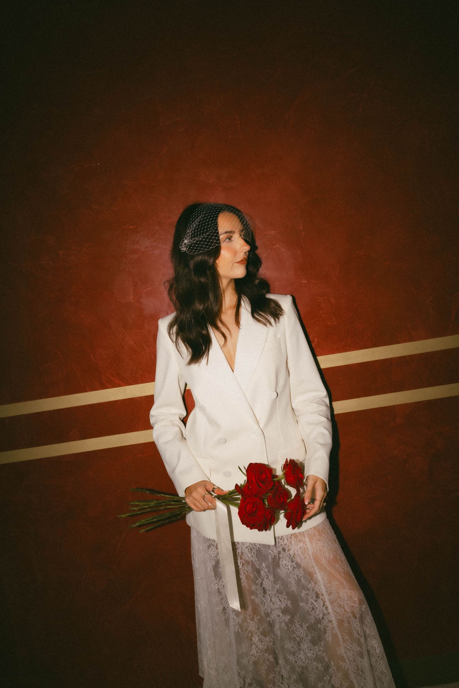 Artistic portrait series against a red backdrop featuring someone in a white blazer holding red roses and making elegant poses.
