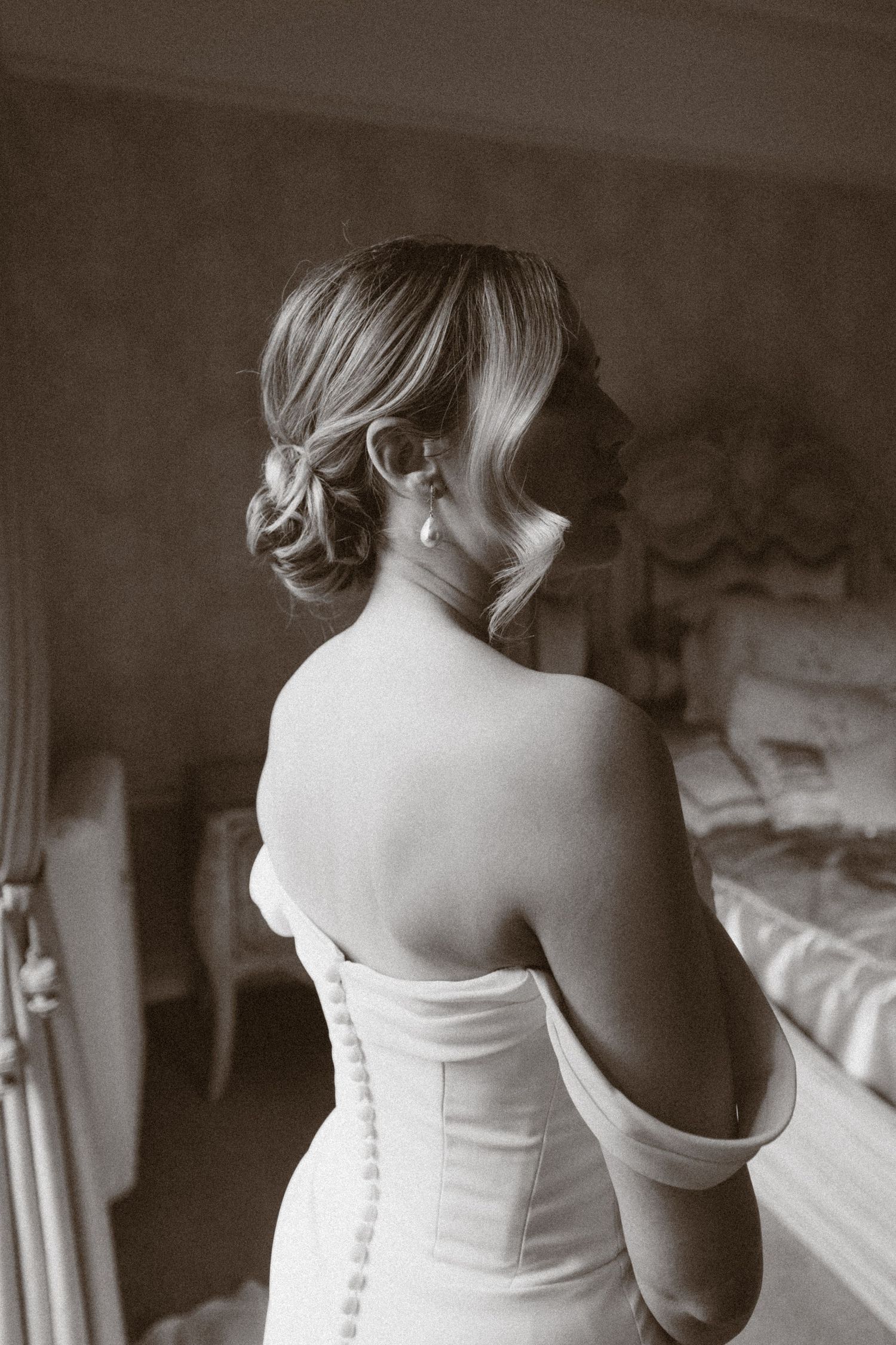 Black and white photo of a bride in a strapless gown with an elegant updo hairstyle and pearl earrings.