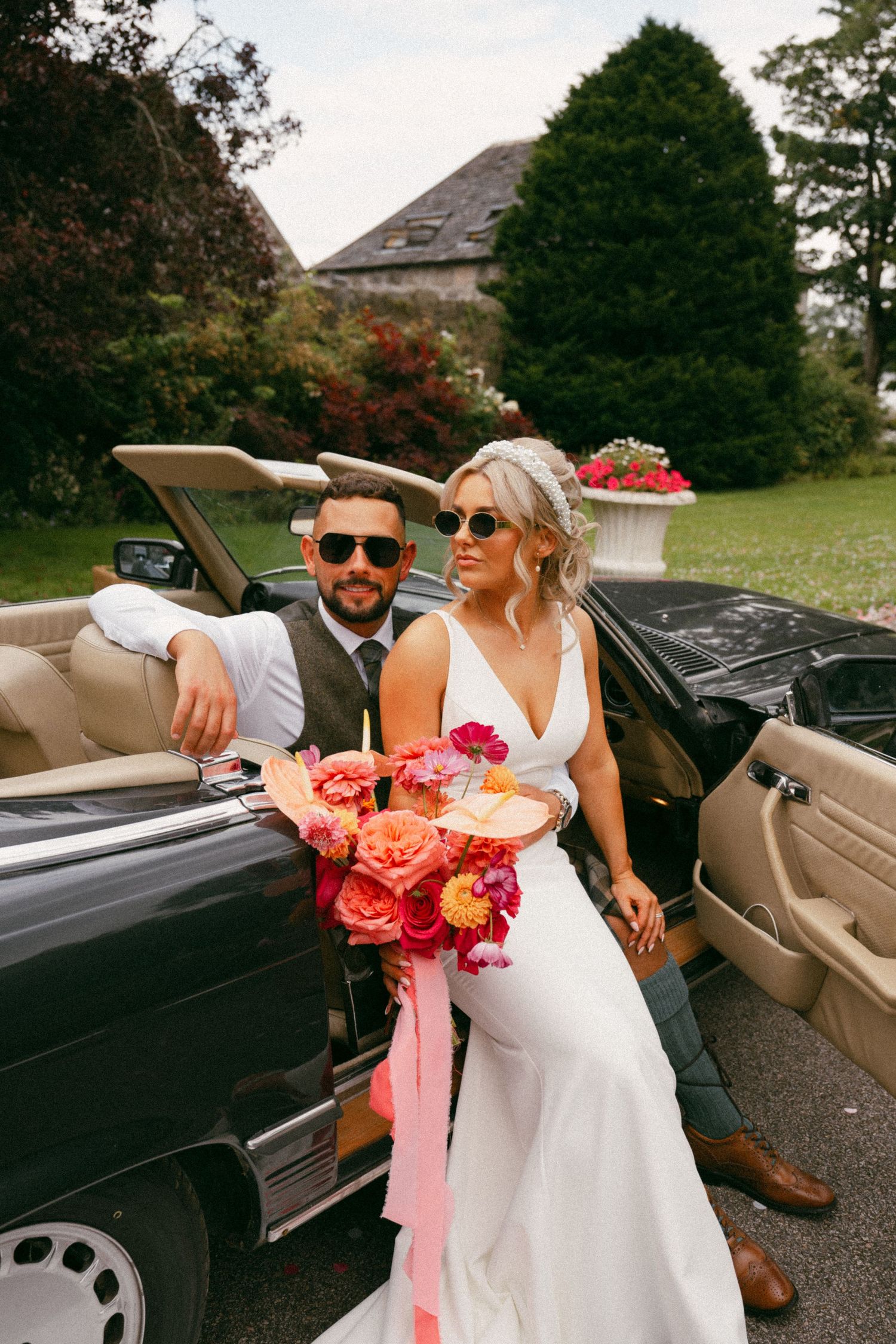 Newlyweds pose with coral bouquet in vintage Mercedes convertible wearing sunglasses. Barra barn, Aberdeen wedding photographer