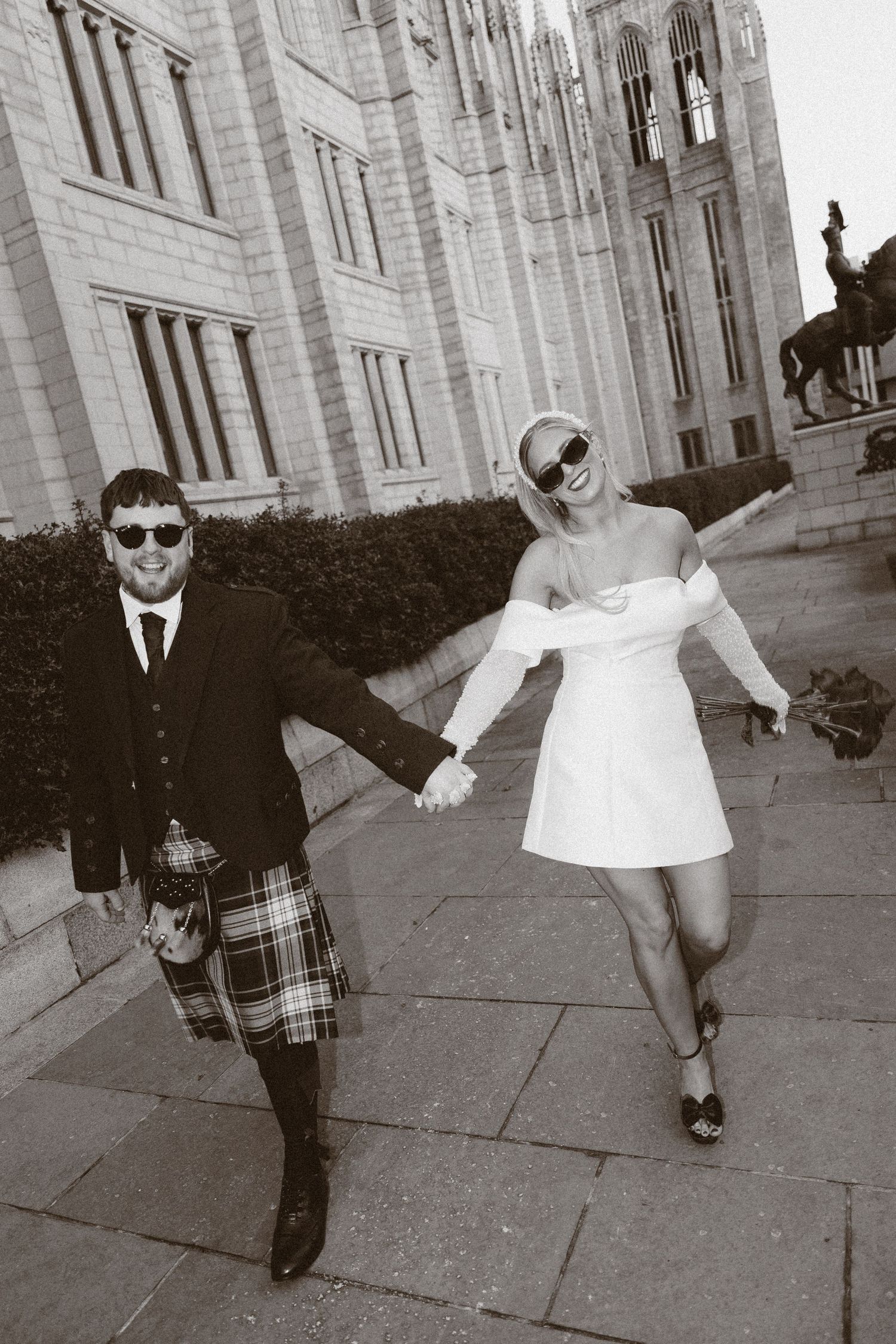 A black and white photo series showing a person in sunglasses and suit performing playful dance moves on a sidewalk.