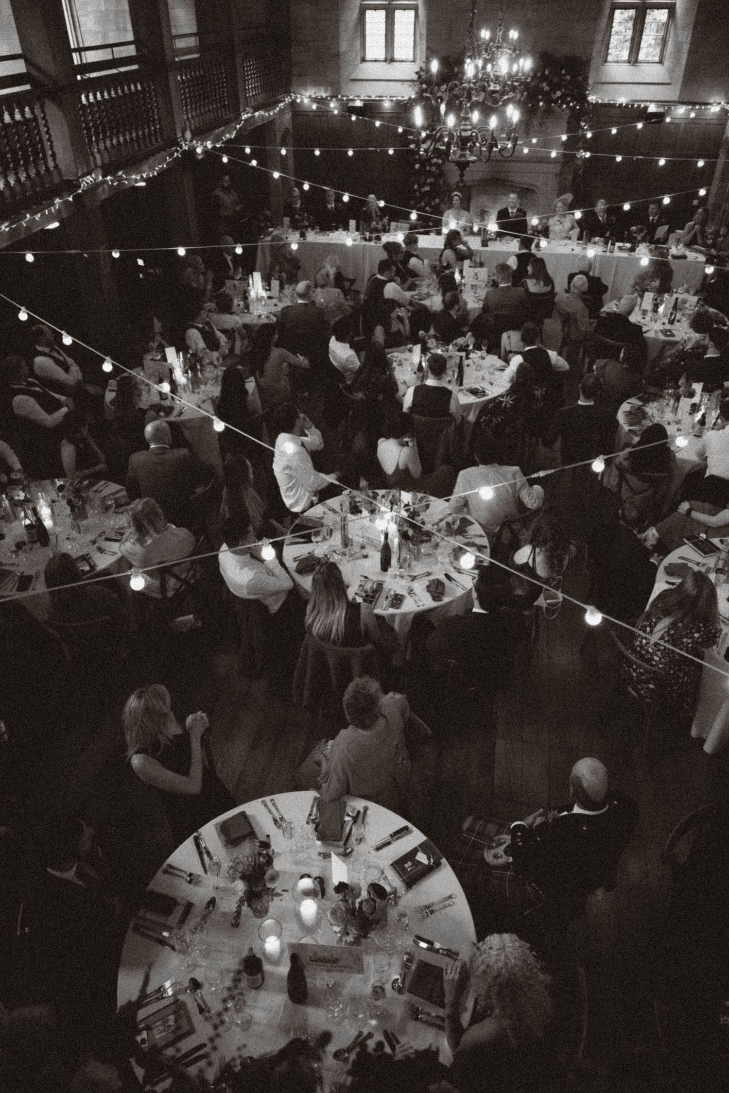 A dimly lit wedding reception venue with tables filled with guests under glowing string lights creating an intimate atmosphere.