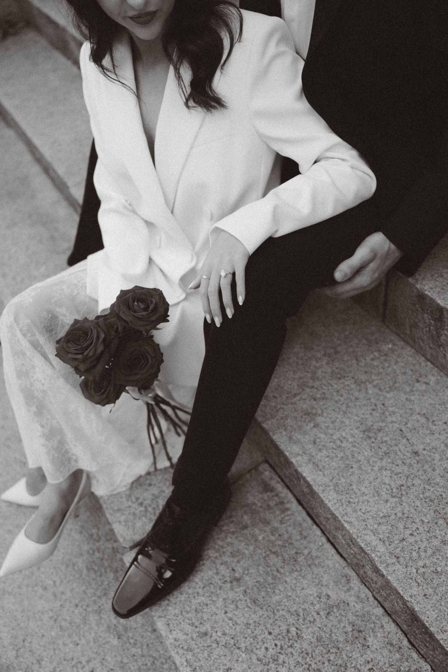 Black and white photo showing formal shoes and red roses on stone steps with white and black clothing details.