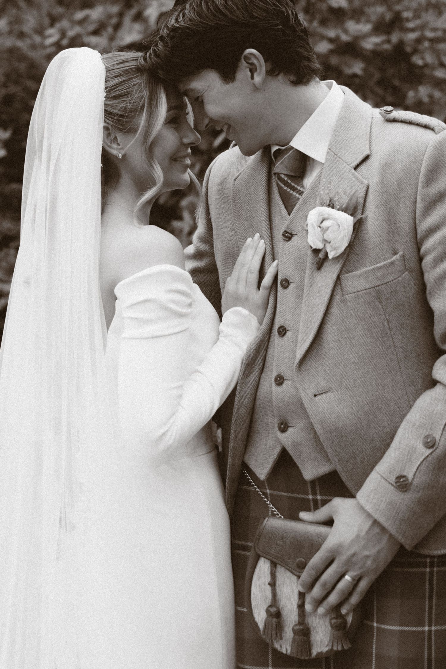 Black and white photo of a bride and groom in Scottish attire sharing an intimate moment on their wedding day.