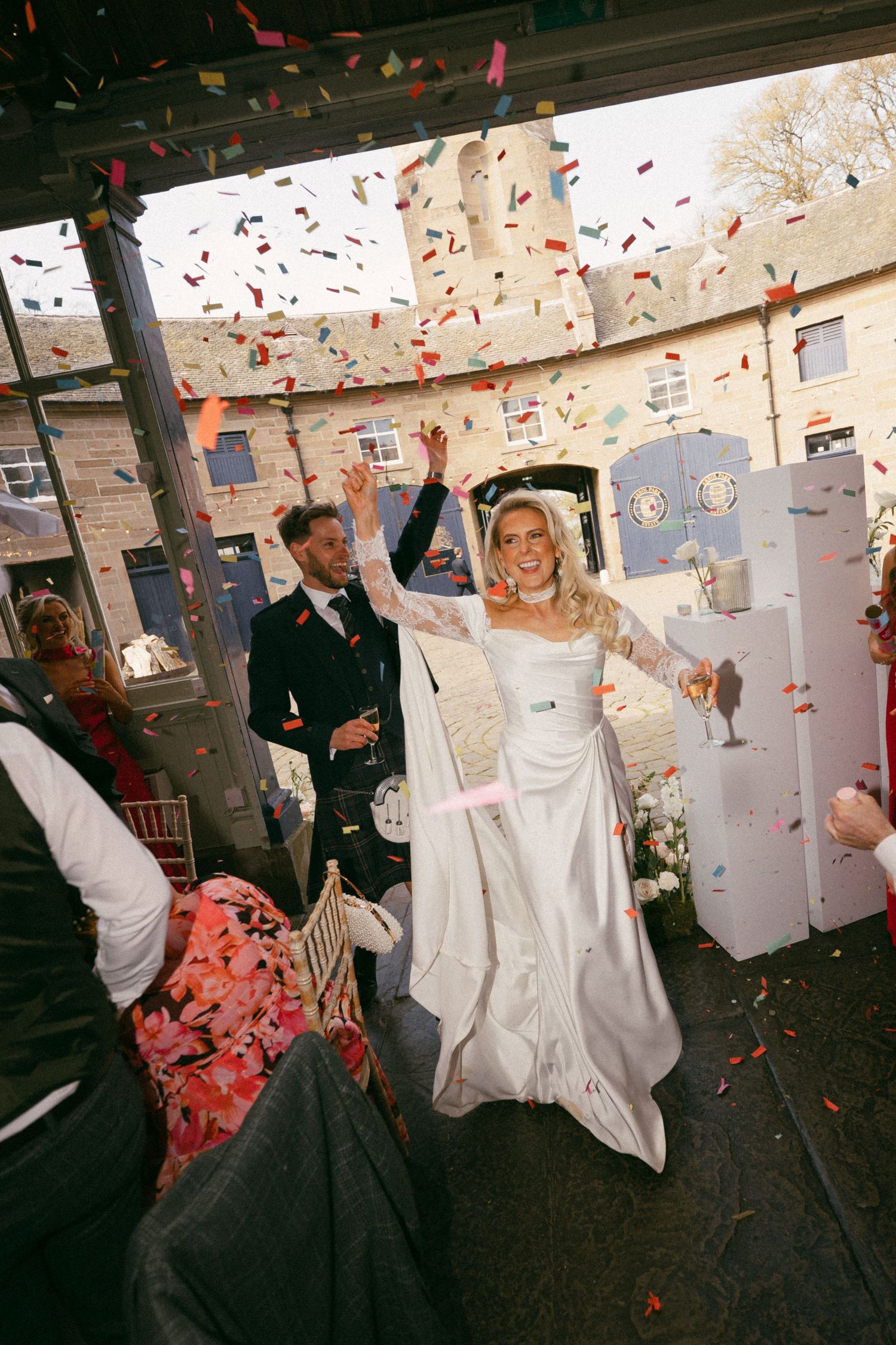 Newlyweds celebrating with confetti during wedding reception as bride in white dress raises arms joyfully. Errol Park Estate Wedding