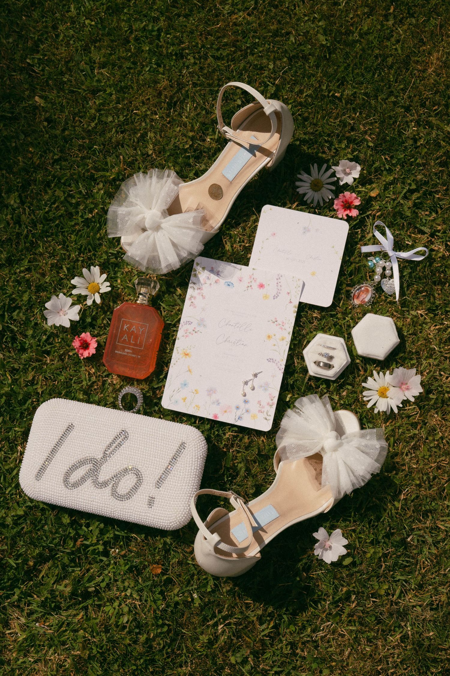 Wedding accessories and decor items arranged on grass including an 'I do' sign, flowers, tulle, and bridal details.