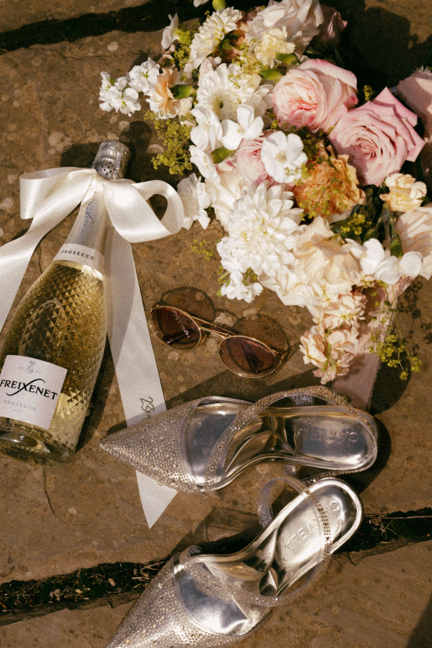 Spilled champagne bottles and scattered floral arrangements create an elegant post-celebration scene on stone flooring.