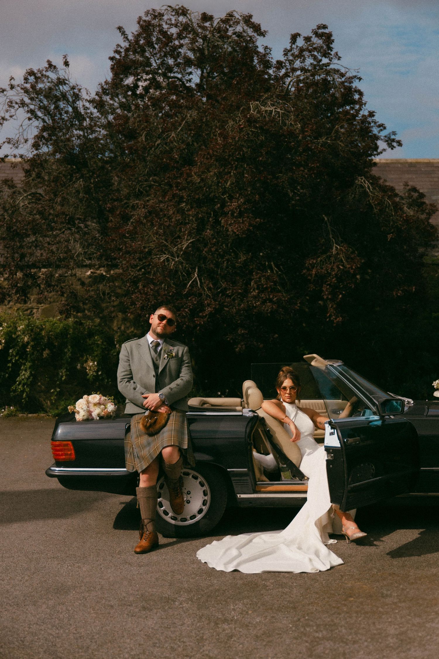 A creative wedding photo sequence showing a couple playfully posing with a vintage black car in a scenic outdoor setting.