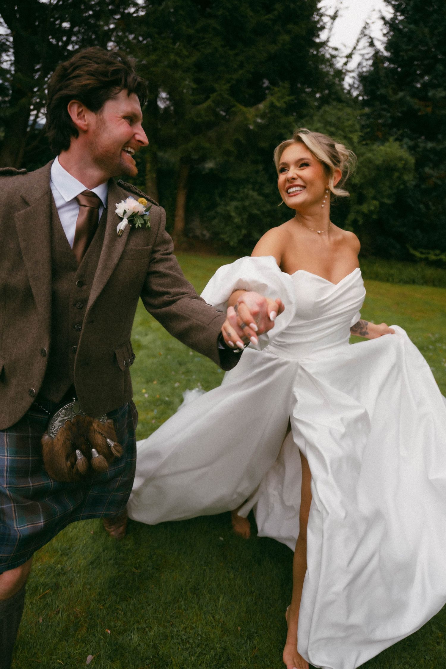 Wedding couple dances playfully together in brown and white attire during outdoor photo session.