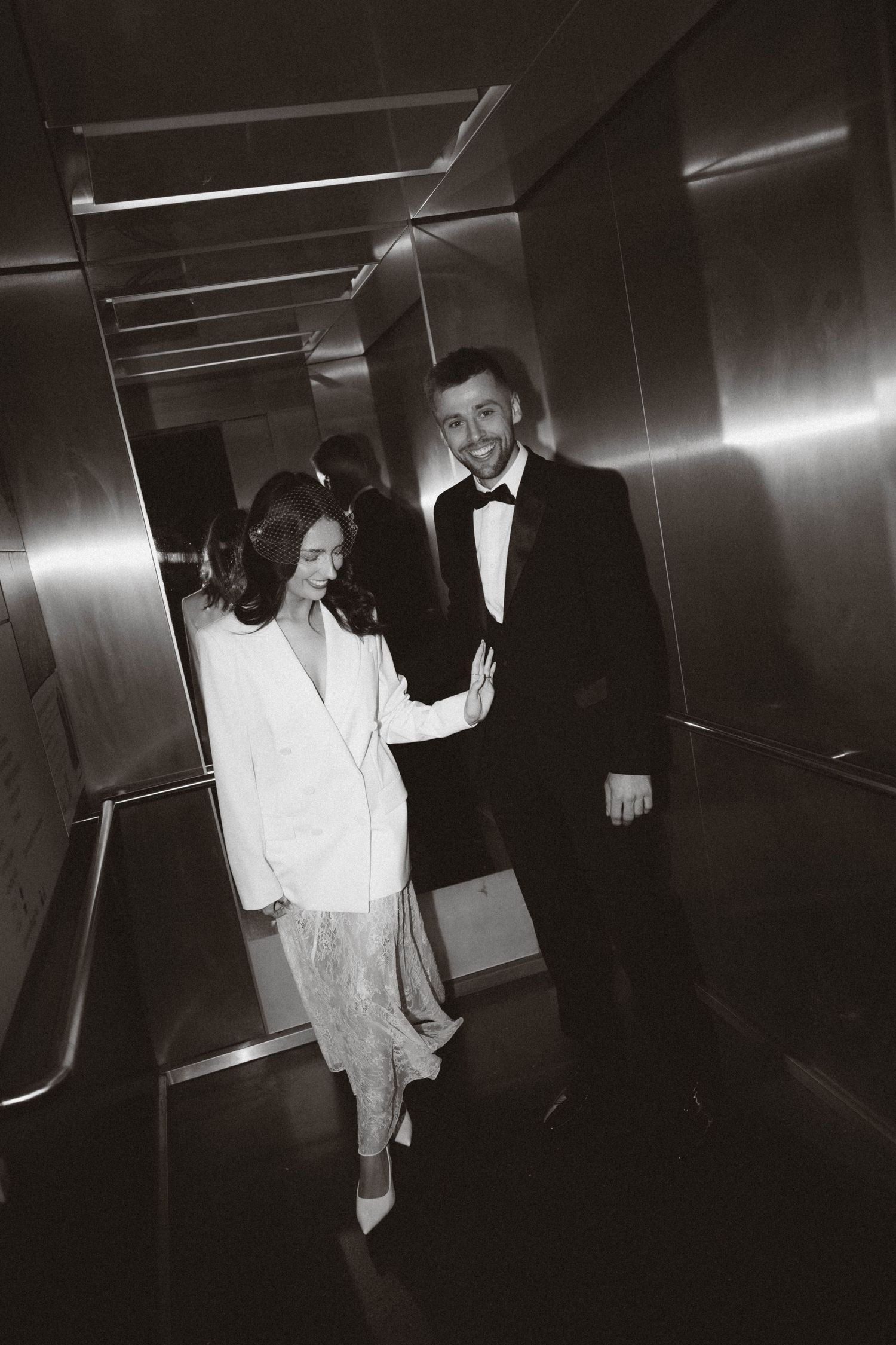 Two figures in dark and light clothing walking through a dimly lit hallway captured in black and white film style.