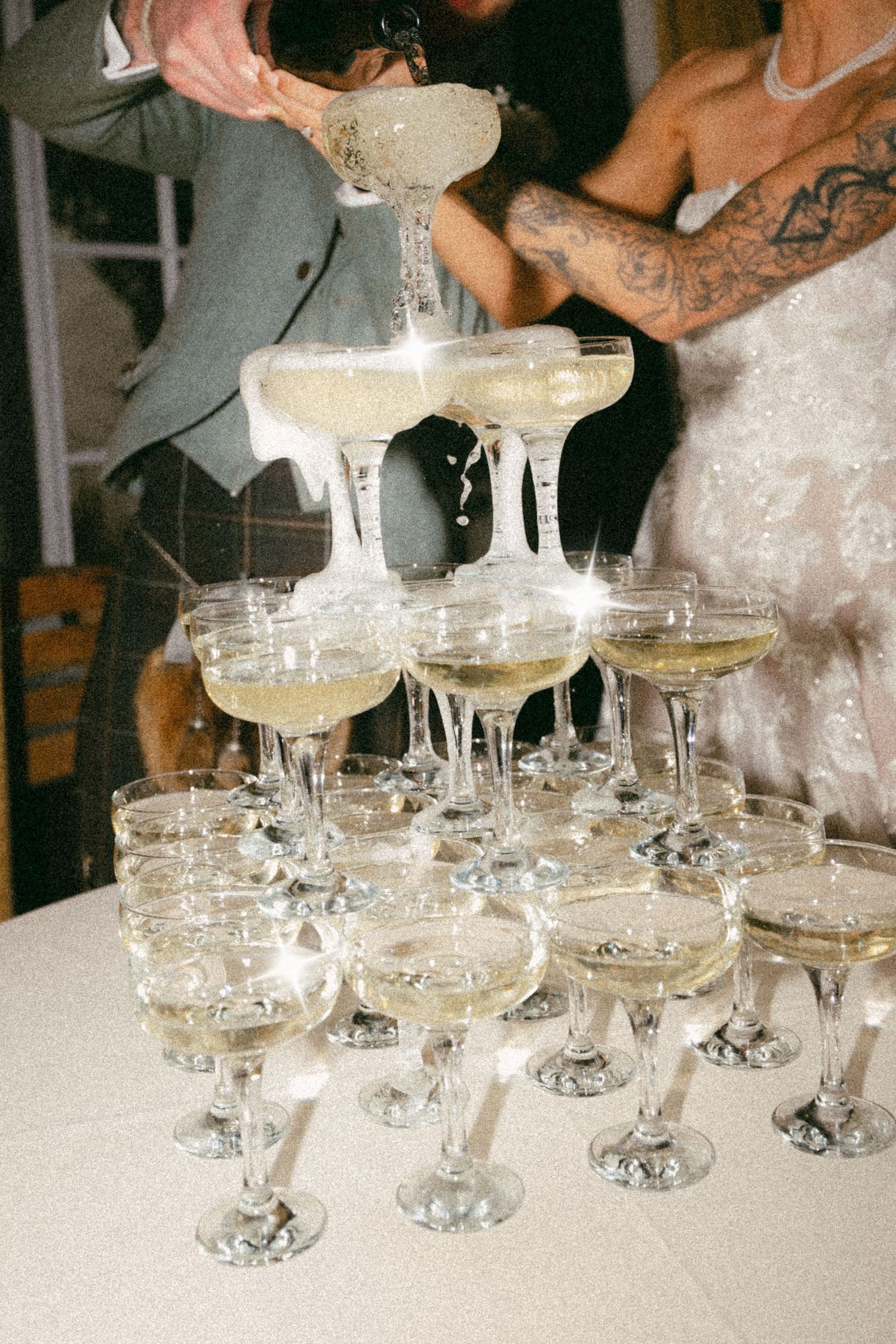 Champagne being poured into a tower of vintage coupe glasses stacked in pyramid formation at an elegant celebration.