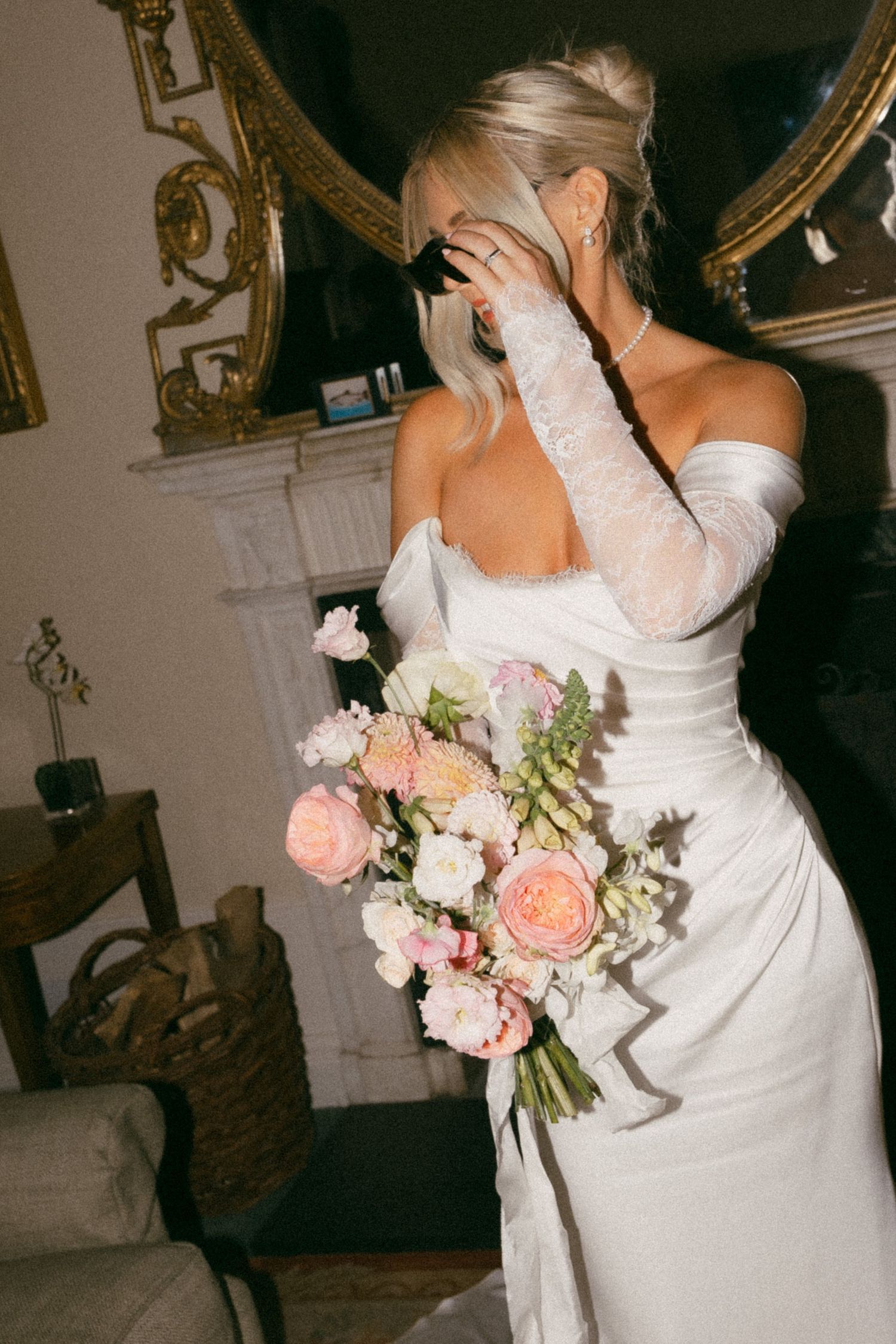 A bride in an elegant white dress holds a soft pink and blush floral bouquet during a wedding reception celebration.