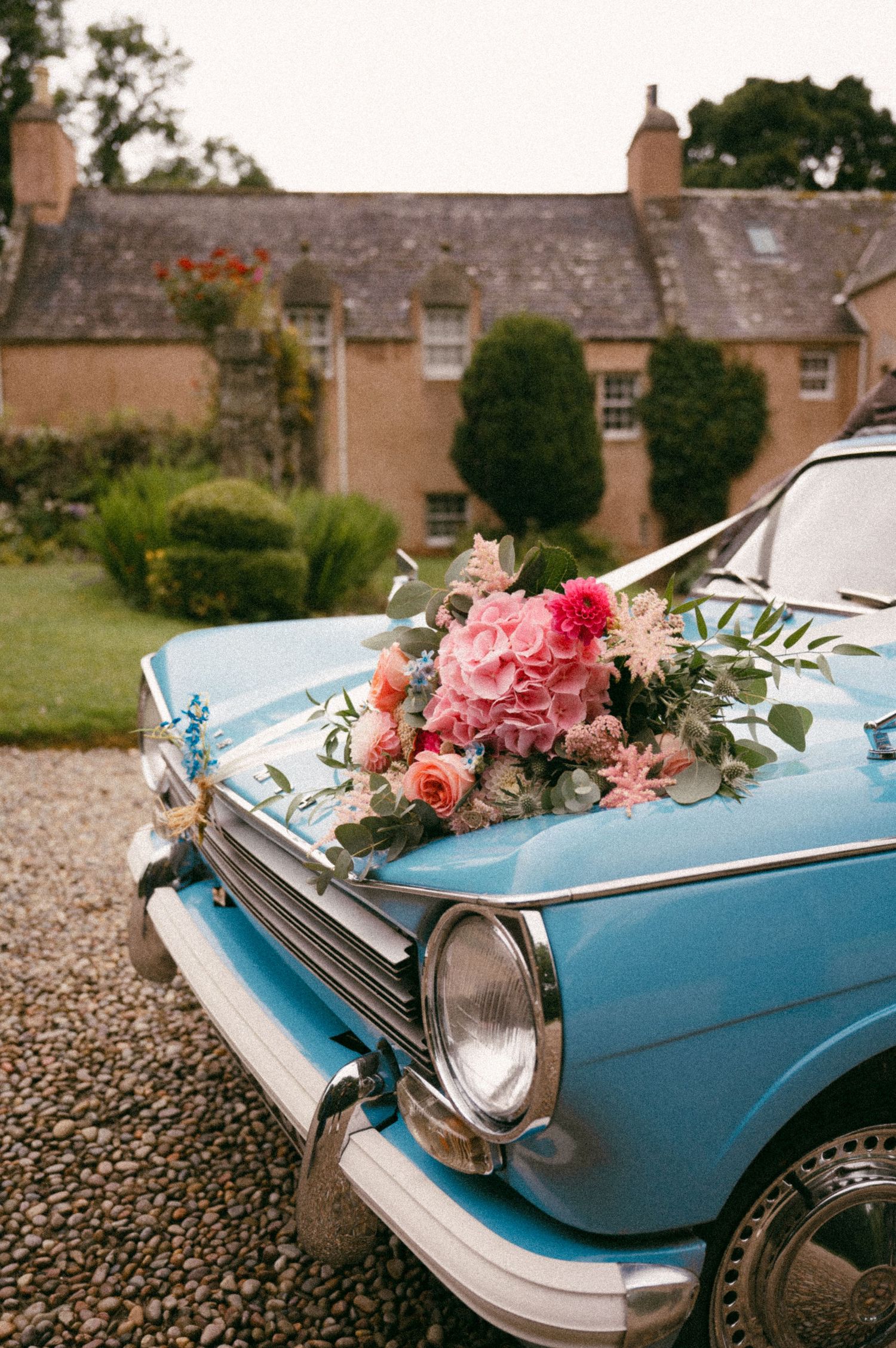 Vintage blue car decorated with pink floral bouquet in front of stone cottage. Aberdeen wedding photographer, Aswanley