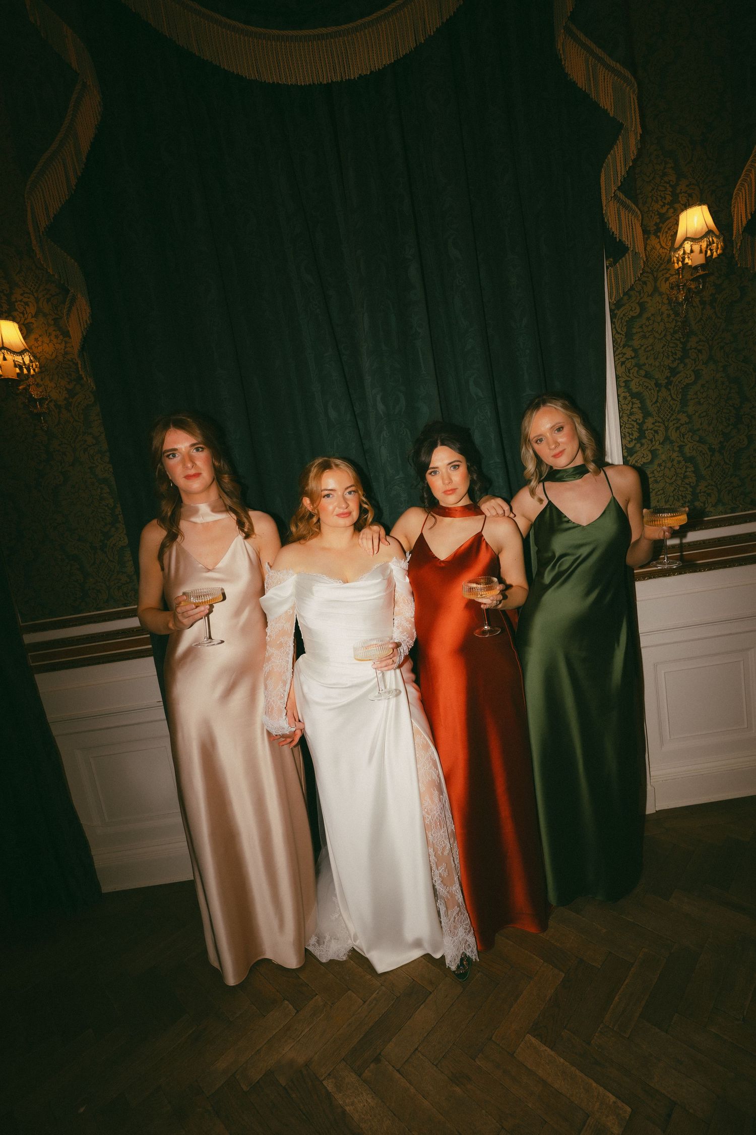 Wedding party in formal dresses dancing together on a dark wooden dance floor.