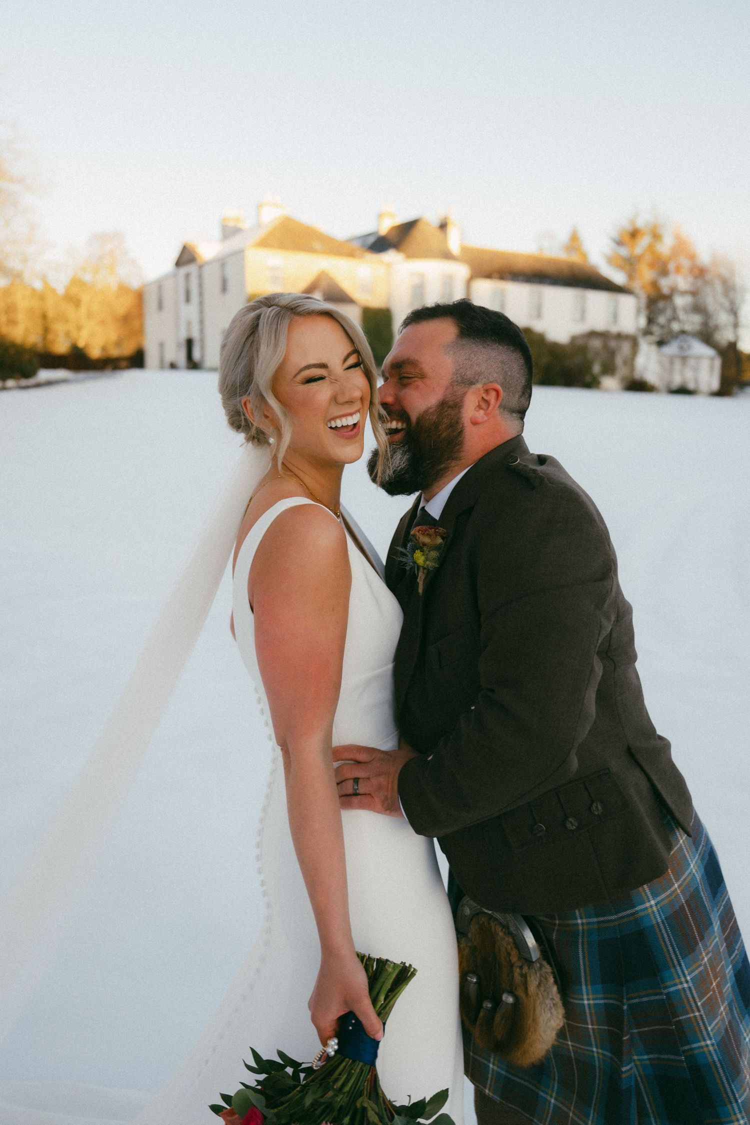A couple in wedding attire share joyful moments together in the snow during their winter wedding photo session.