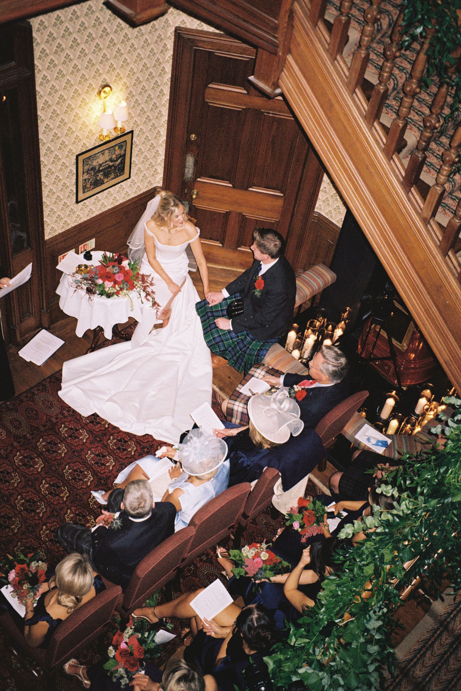 Overhead view of a wedding ceremony in a historic venue with wooden paneling, floral decorations and patterned carpet.