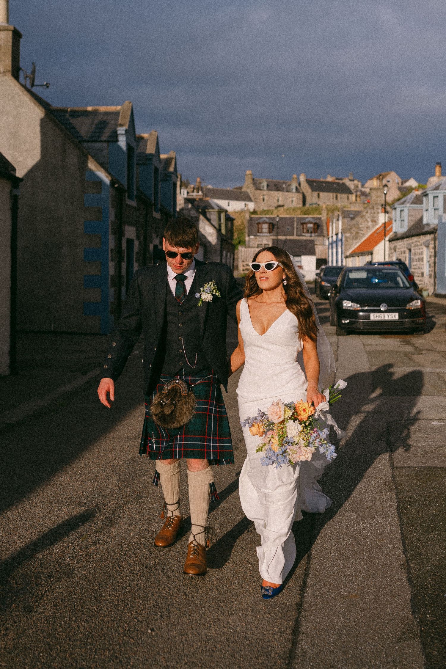 Couple walking down Scottish street, groom in kilt and bride in flowing dress.  Aberdeen wedding photographer, sea field arms hotel Cullen