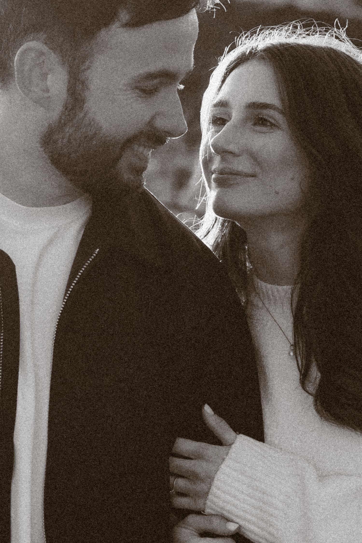 Black and white photo of a smiling couple sharing a tender moment, woman wearing a white sweater and diamond engagement ring.