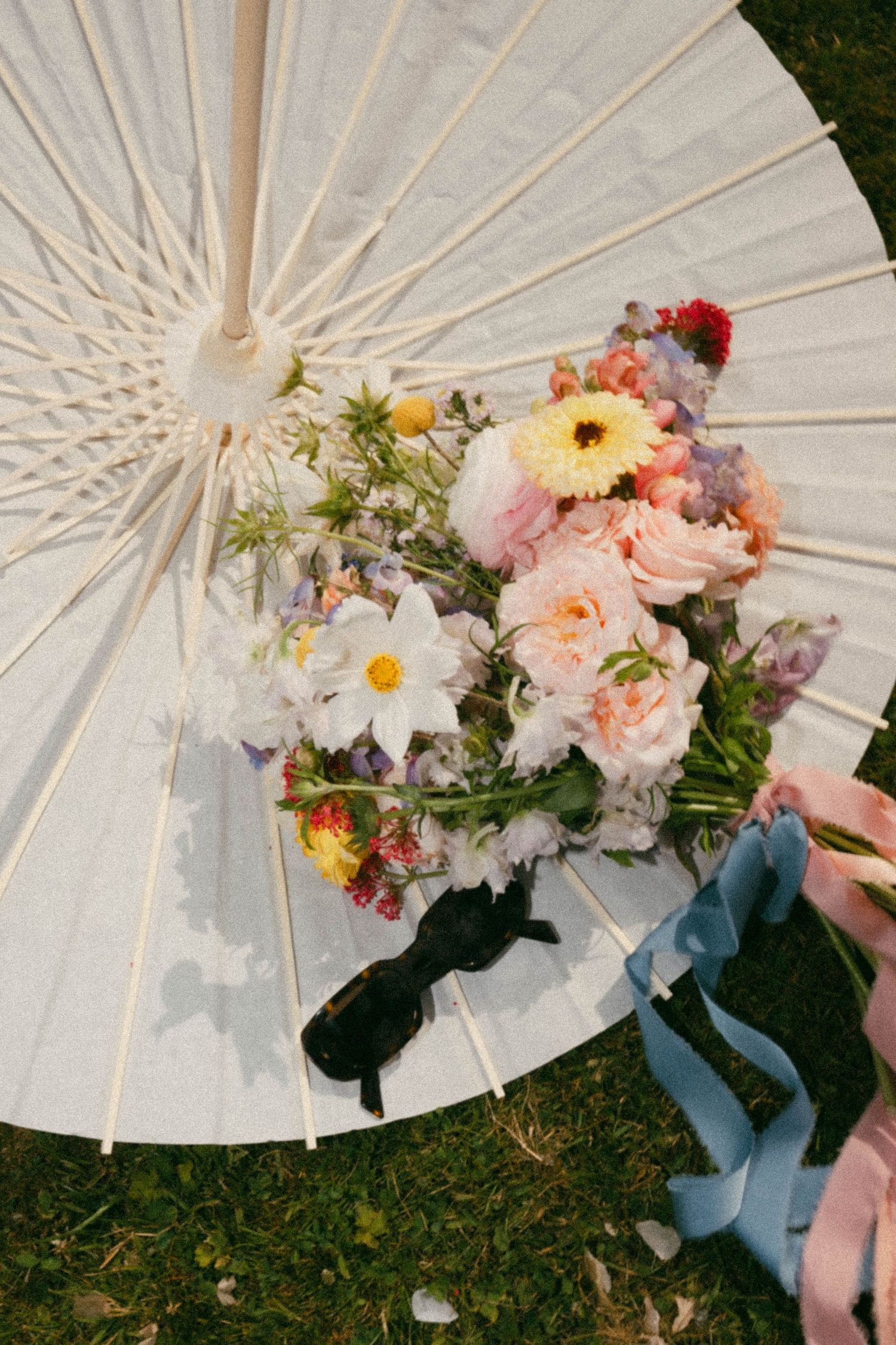 A delicate bouquet of mixed flowers including roses, daisies and gerberas rests on a white parasol on grass.