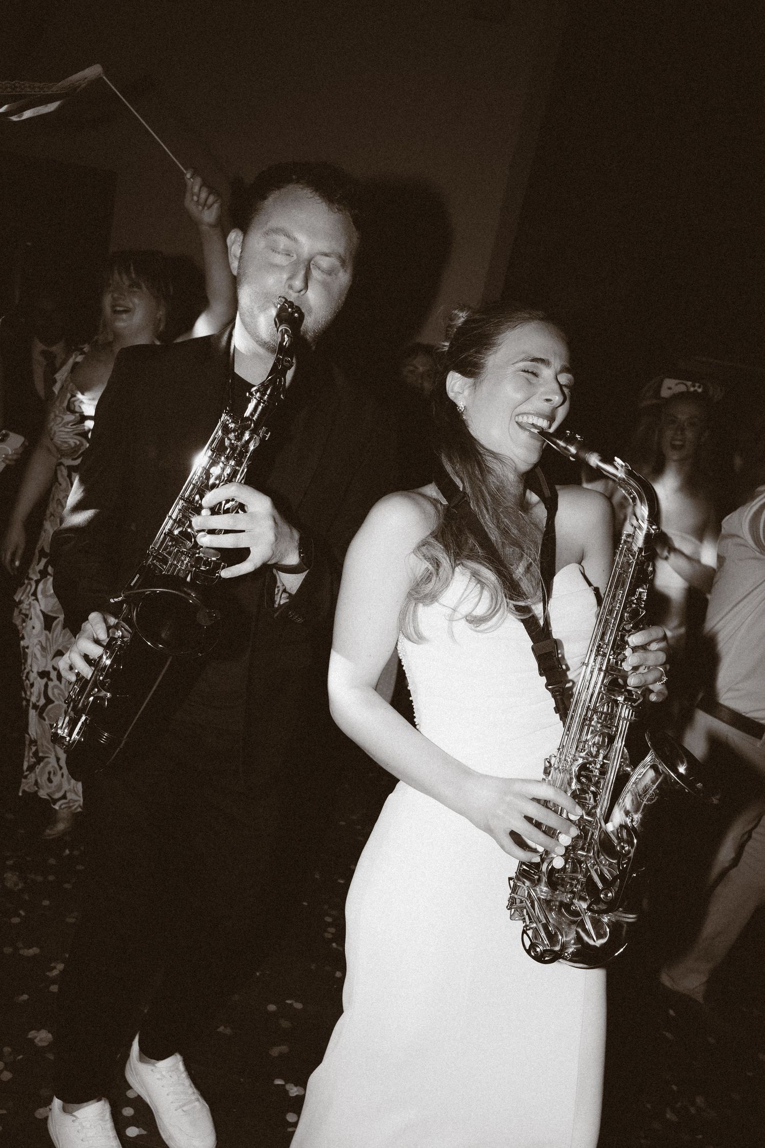 Black and white photo of a bride and groom playing saxophones together at their wedding reception.