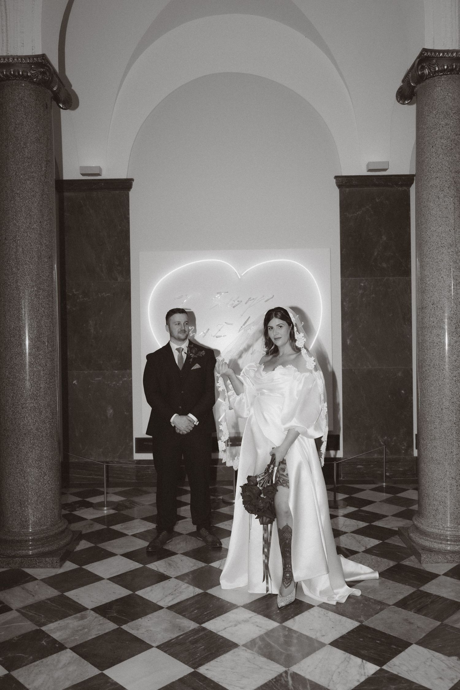 Black and white wedding photos show a couple and guests in a grand hallway with checkered floors and arched columns.