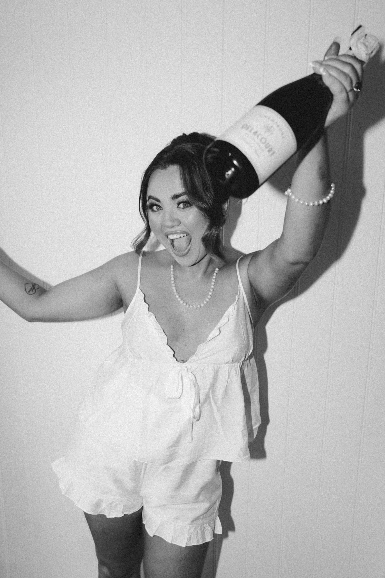 Black and white photo series showing figure in white blouse and pearl necklace striking dynamic poses against plain wall.