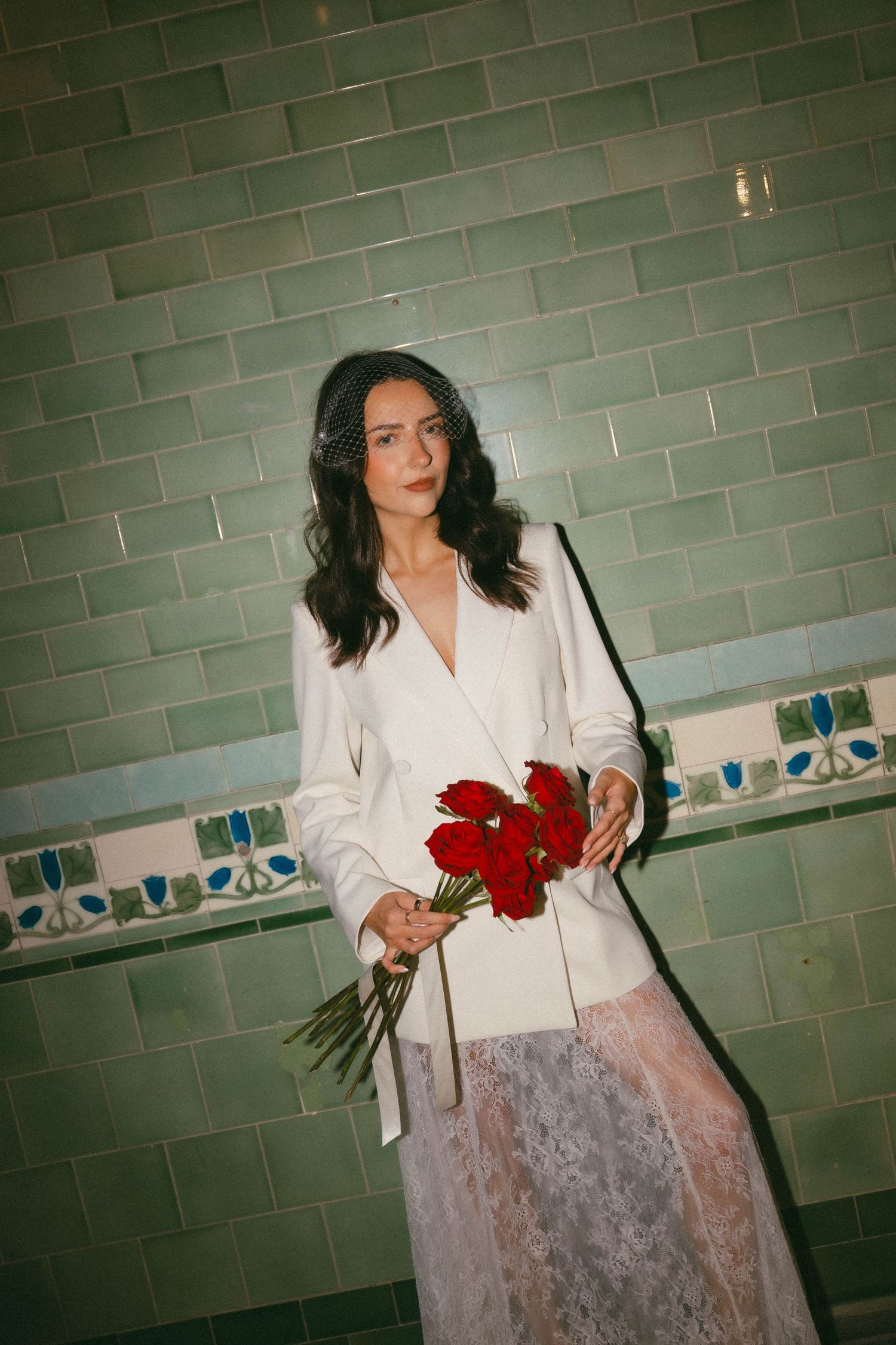 A person in a white blazer holding red roses poses against a green tiled wall in multiple sequential shots.