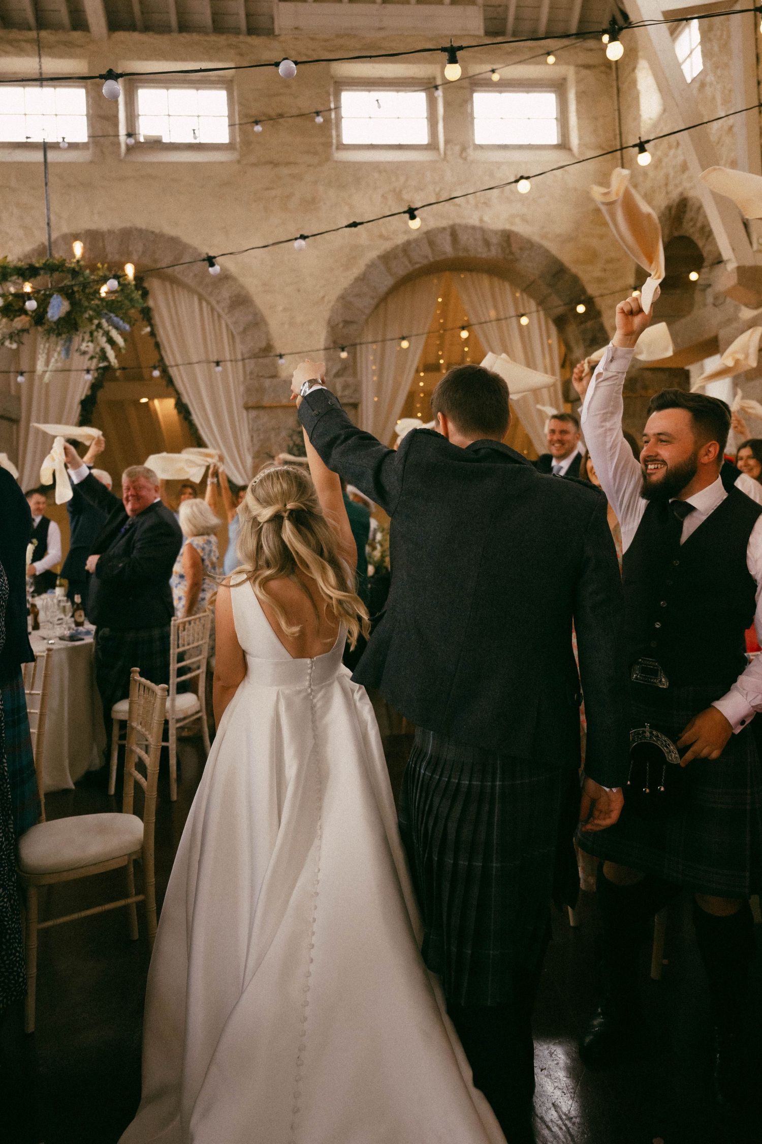 Guests celebrate at a rustic indoor wedding reception with string lights and stone archways as decor.