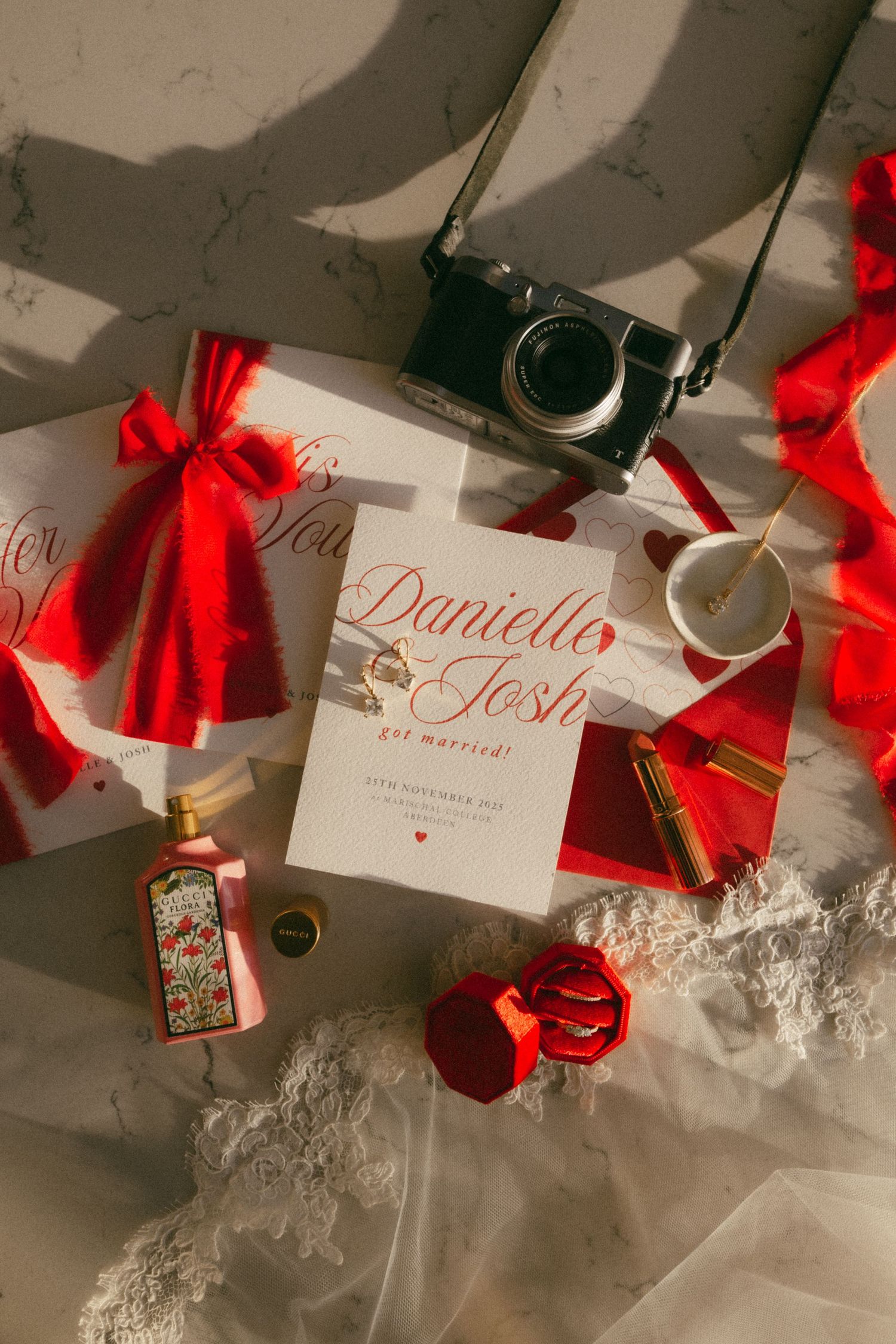 Elegant wedding place cards with red ribbons and calligraphy names displayed alongside scattered rose petals and decor.