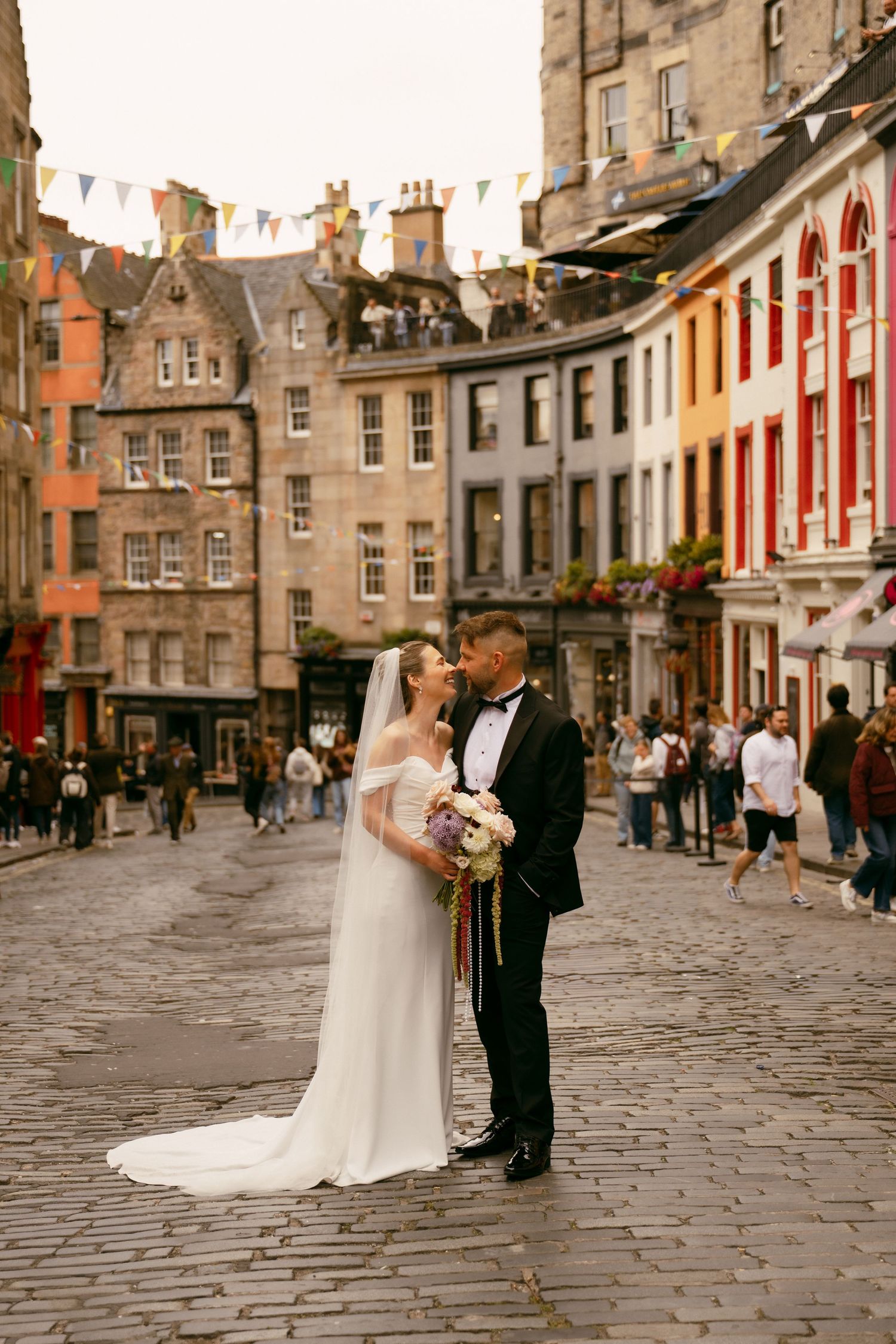 Bride and groom share a romantic moment on cobblestone street in Edinburgh's historic Victoria Street.