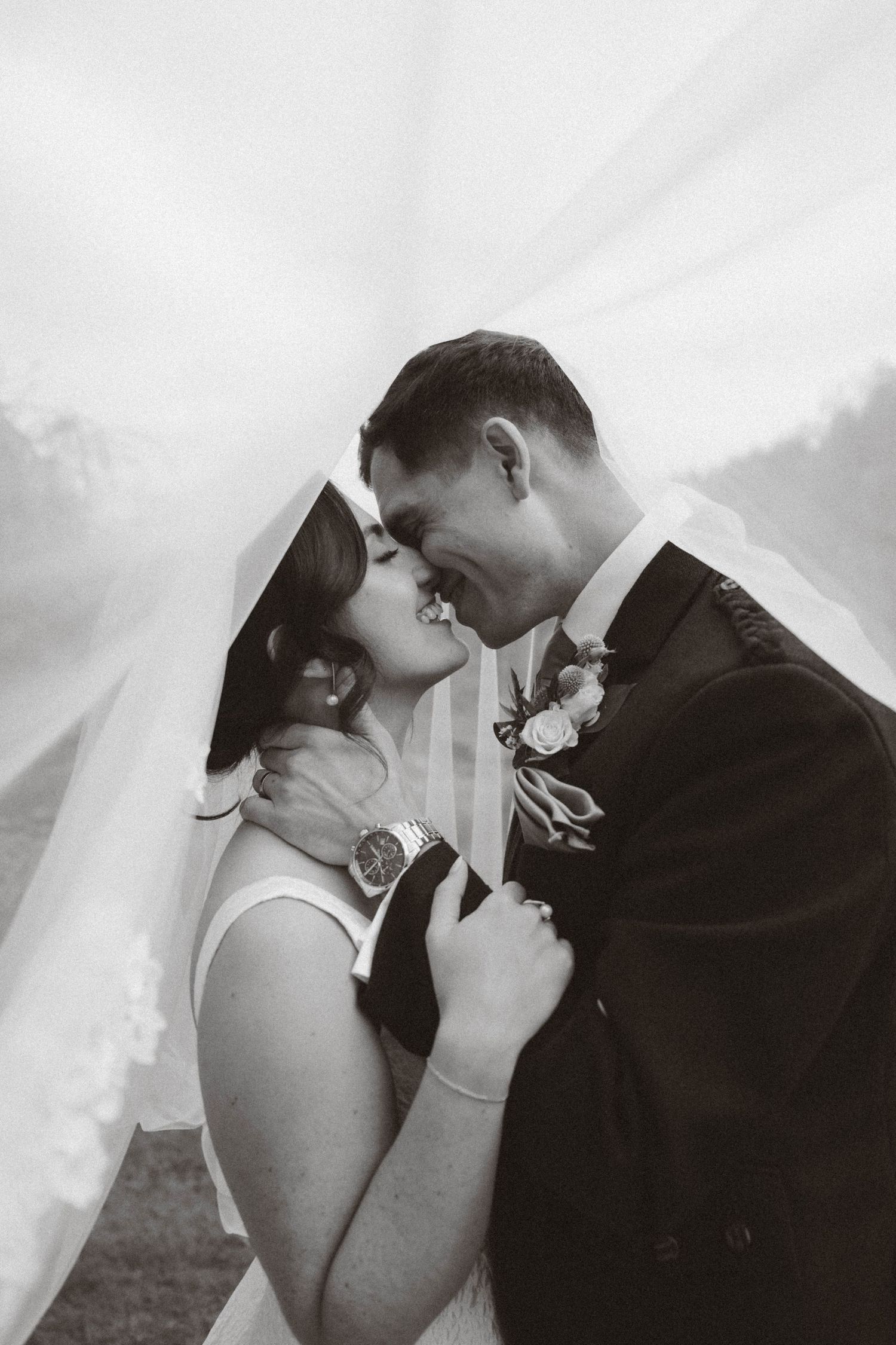 A romantic black and white wedding portrait of a couple sharing an intimate moment under a veil.