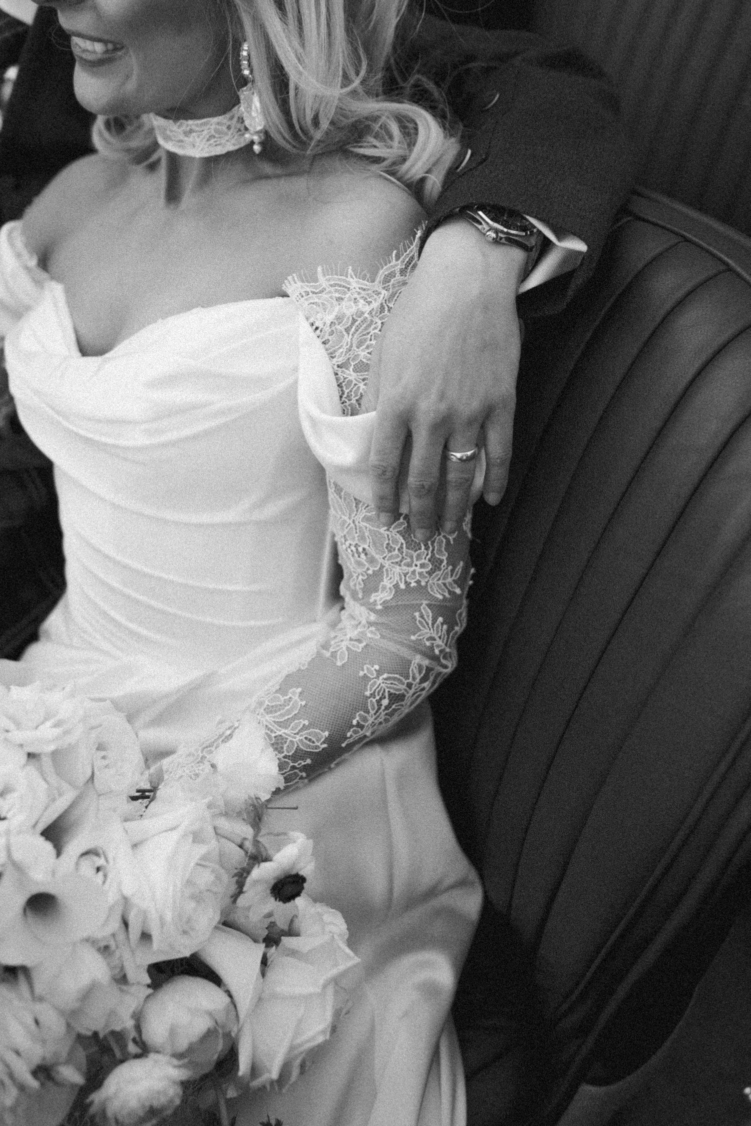 Close-up detail of a bride's lace wedding dress and ring while seated in a vintage car.