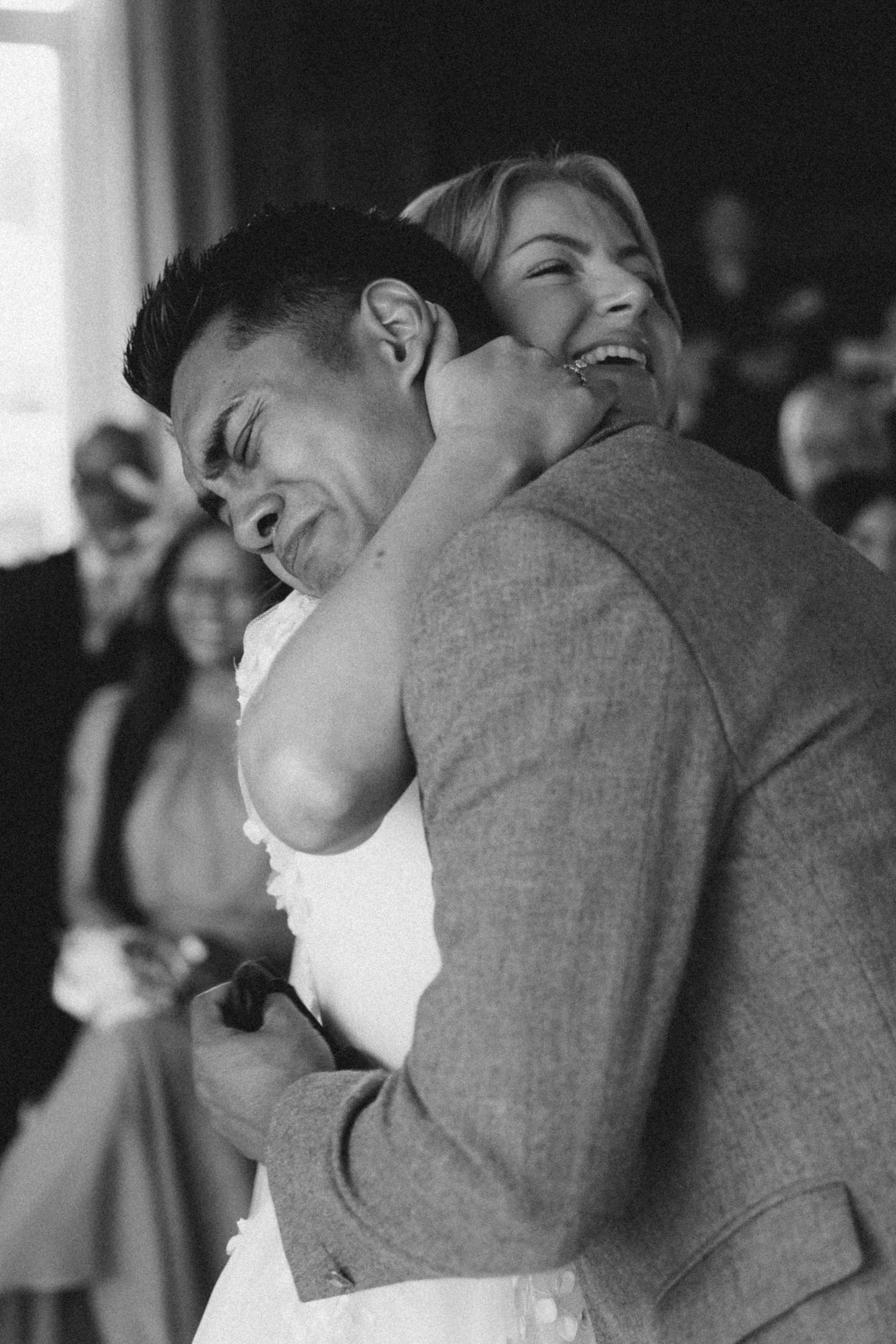 A joyful black and white wedding moment captured as a couple embraces in laughter during their celebration.