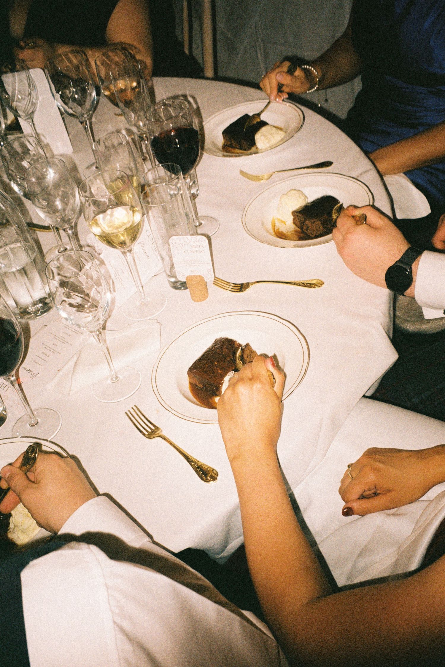 Overhead view of a dinner table with wine glasses and plates during a meal at a restaurant with white tablecloth.